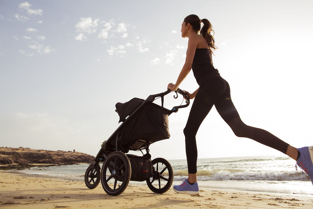 Young mom is running with stroller on the beach. Reprise course post-partum